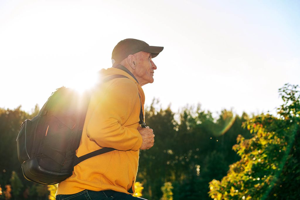 senior man with black backpack hiking exercise in mountain side view