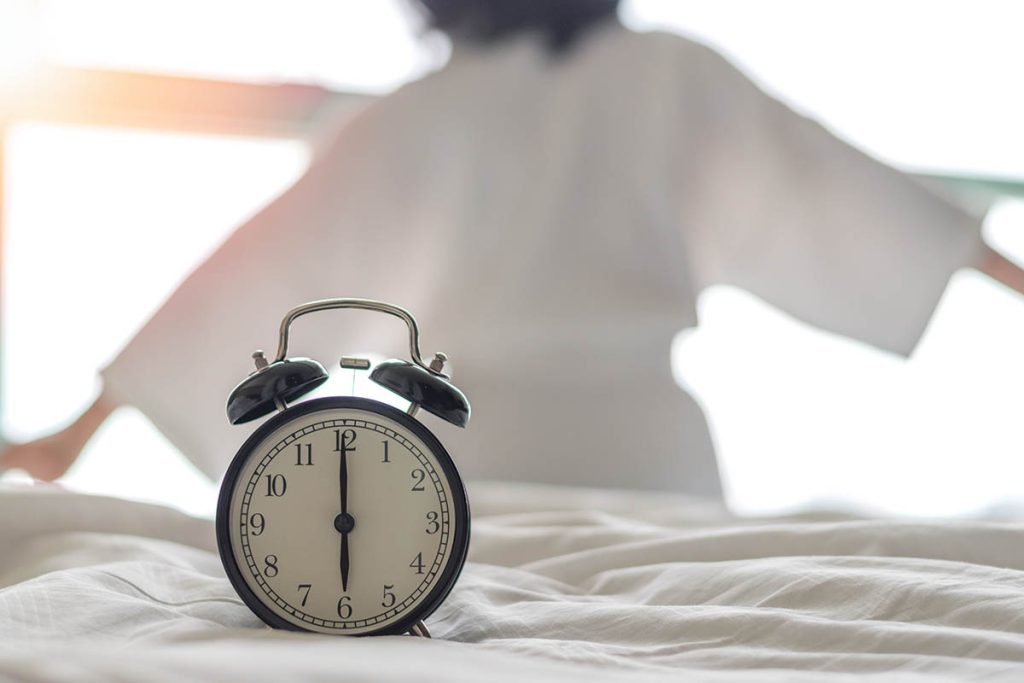 Woman on bed wake up stretching in bedroom with alarm clock 