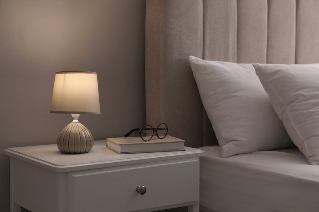lamp, book and glasses on bedside table indoors. Bedroom interior elements