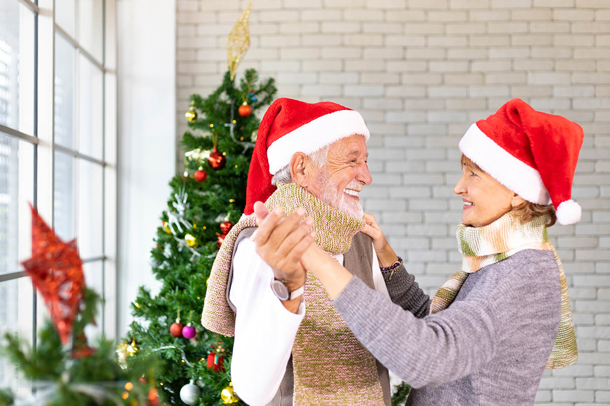 Senior couple dancing and smiling together in happiness during Christmas holiday while wearing Santa hat for season celebration