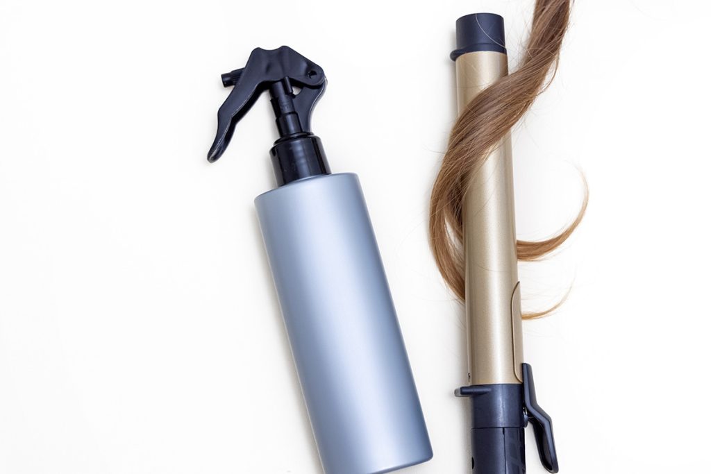 Hair protectant spray, hair tool, and brown hair on white background