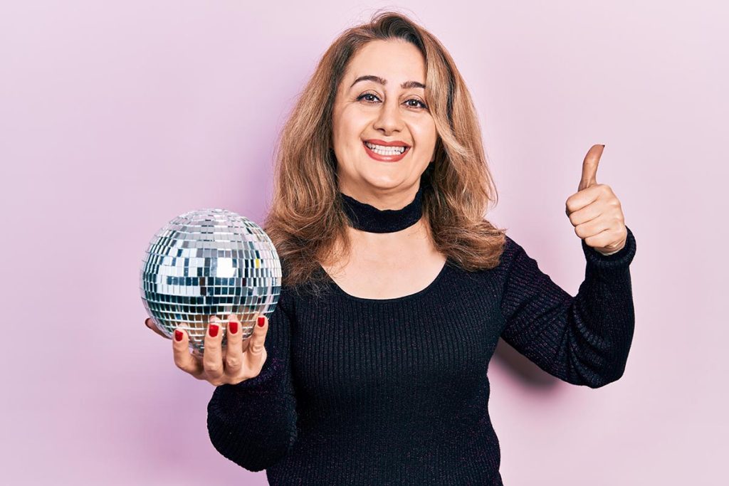 Middle age woman holding shiny disco ball smiling and thumbs up