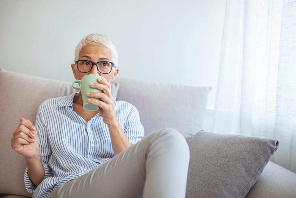 Shot of a mature woman relaxing on the sofa at home with a cup of coffee. Coffee and a quiet moment. Happy mature woman with coffee cup relaxing by the window