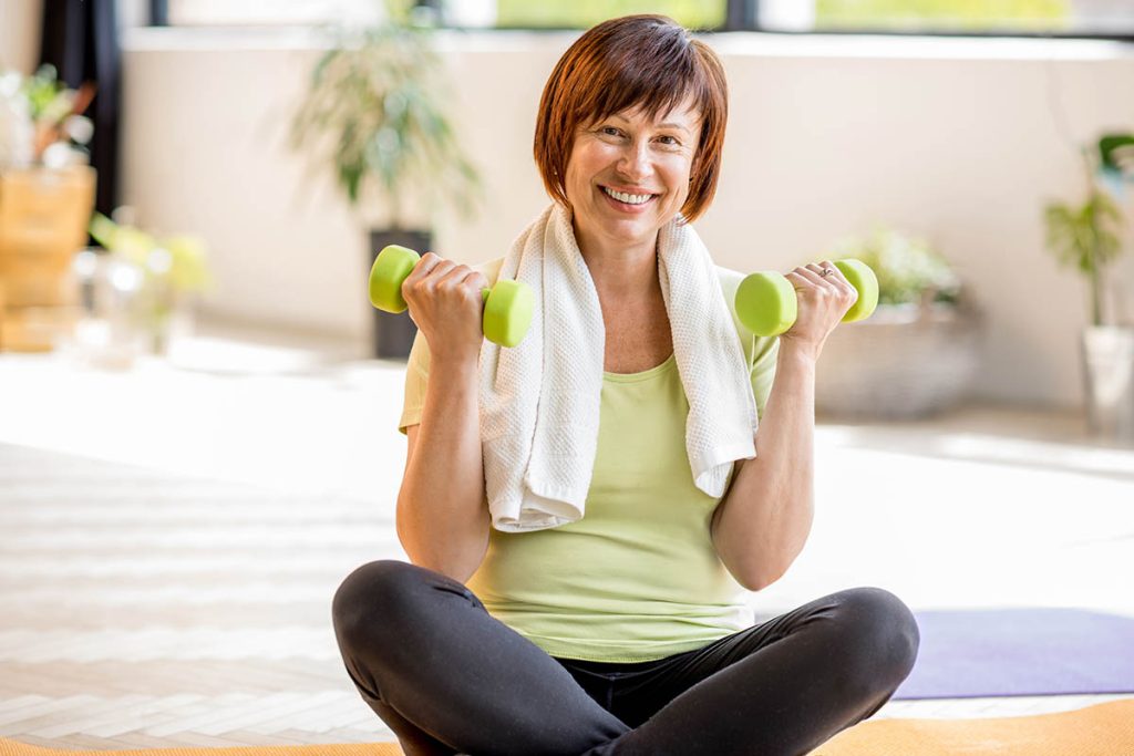 older woman in sportswear exercising with dumbbells indoors at home or gym