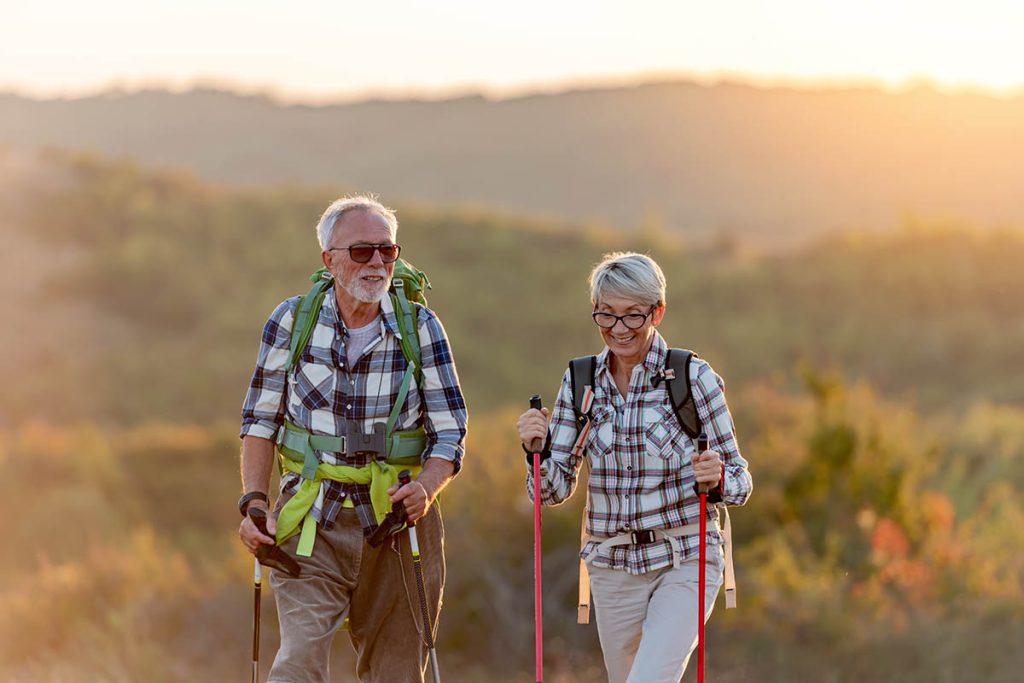 Active senior couple hiking in mountains with backpacks and hiking poles, enjoying their adventure