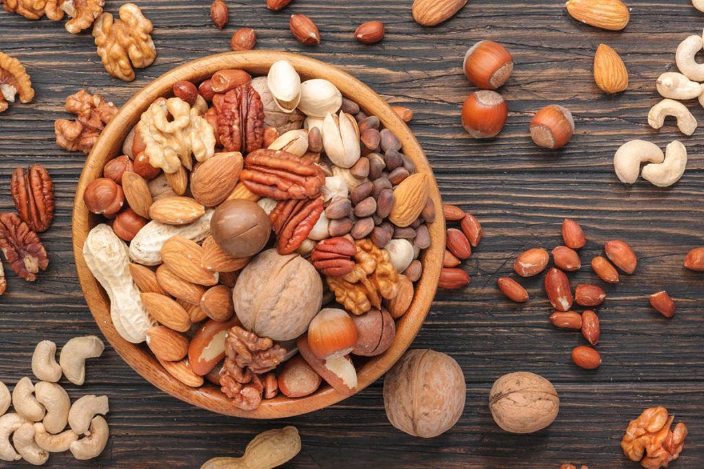 Assortment of nuts in bowls. Cashews, hazelnuts, walnuts, pistachios, pecans, pine nuts, peanuts, macadamia, almonds, brazil nuts. Food mix on wooden background, top view, copy space