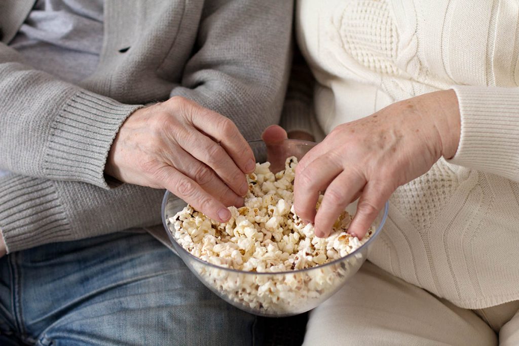 Two aged people eating popcorn together.Hands of elderly people reaching into bowl of popcorn.