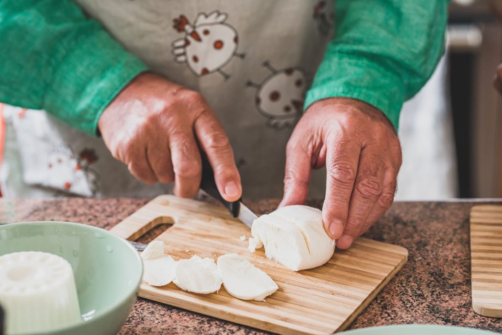 close up of hands of mature man and senior cutting a mozzarella with a knife and cooking food to eat