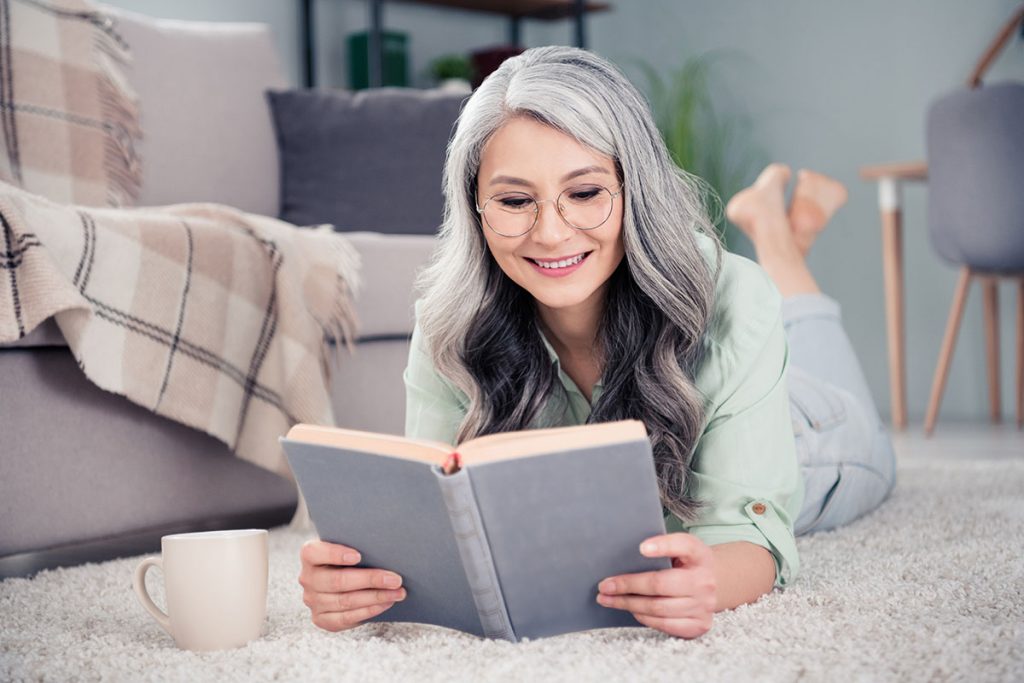 mature woman lying on the floor happy reading her book