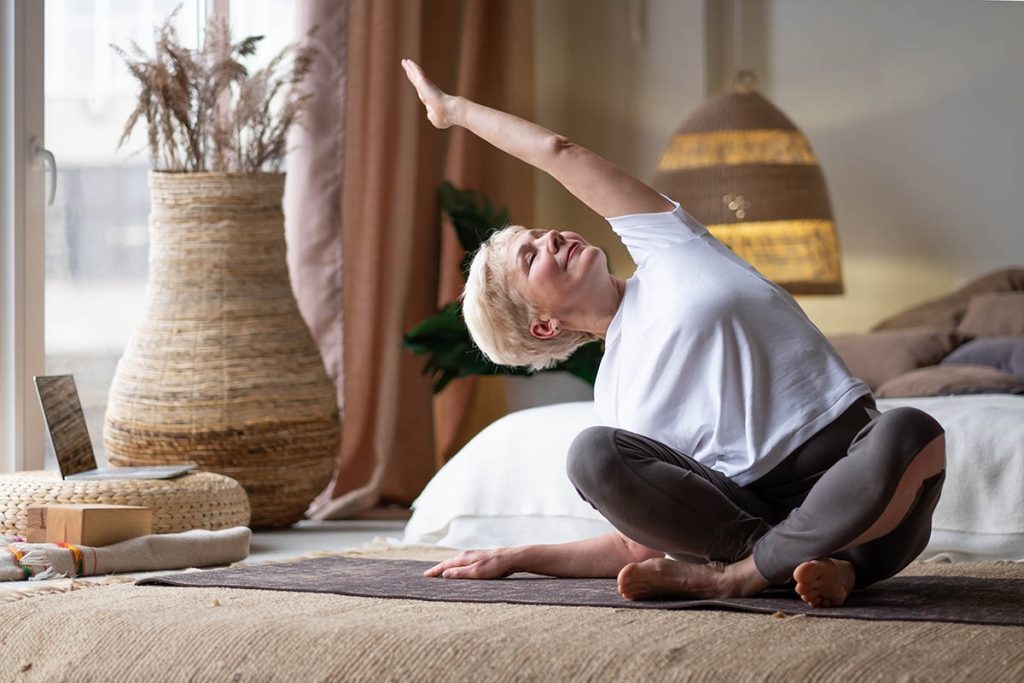 Mature Woman doing stretching yoga side bend at home.