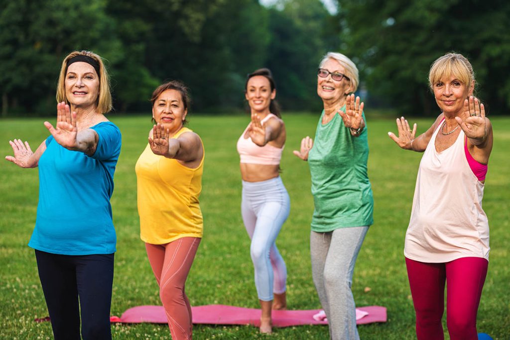 Multiethnic group of senior women training at park with fitness instructor
