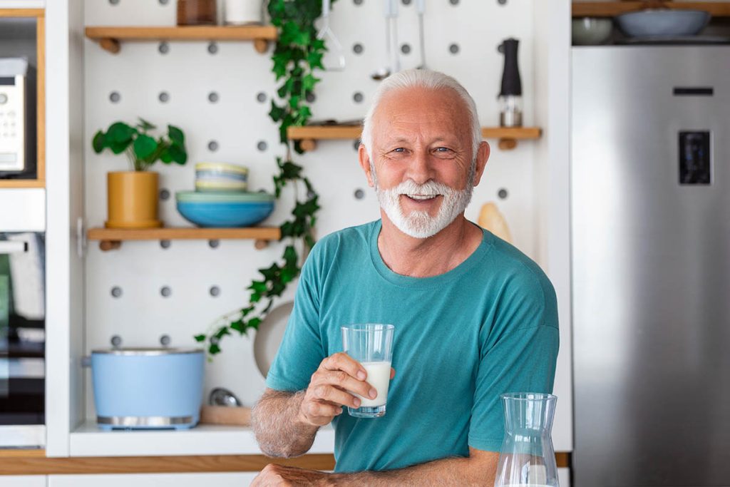 Senior man drinking a glass of milk with a happy face standing and smiling.