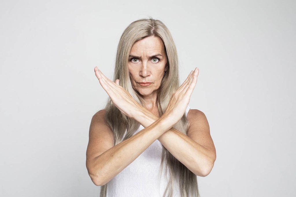 Senior woman with long gray hair wearing casual style rejection expression crossing arms doing negative sign, angry face over grey background. 