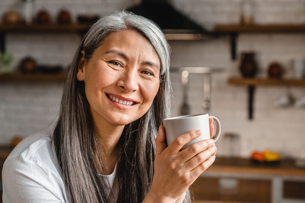 Cheerful woman with grey hair drinking tea in the kitchen