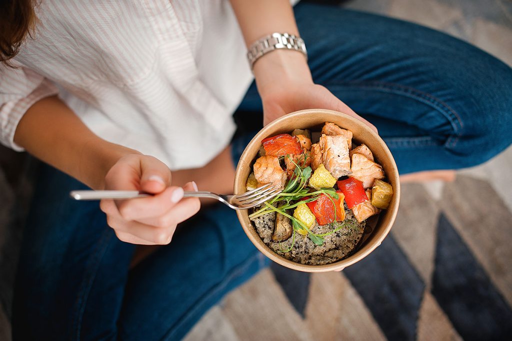 Girl holds a paper plate with healthy food sitting on the floor. Home delivery food. Healthy eating concept. 