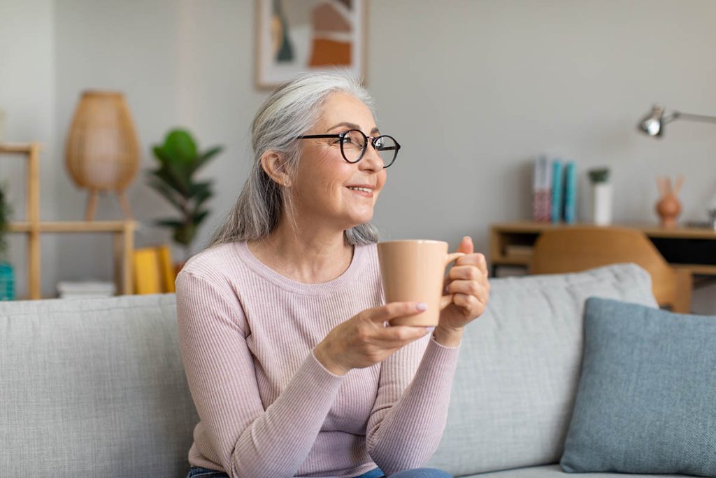Happy older woman drinking a mug of coffee on her couch