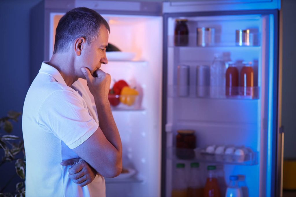 Hungry mature man near open fridge in kitchen at night