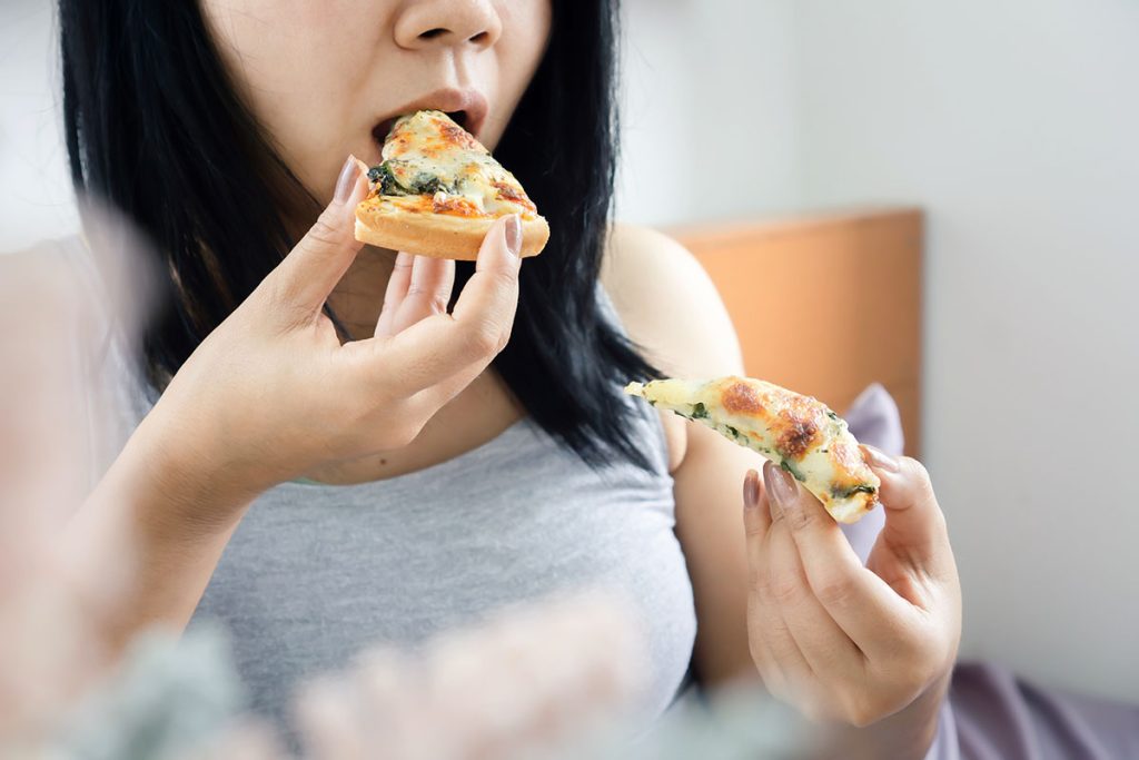 woman overeating pizza sitting in bed late at night before bedtime  unhealthy eating, lifestyle concept