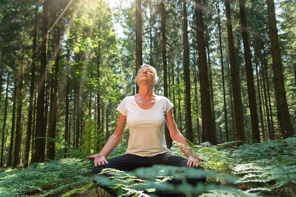 older woman meditating in the forest. forest bathing