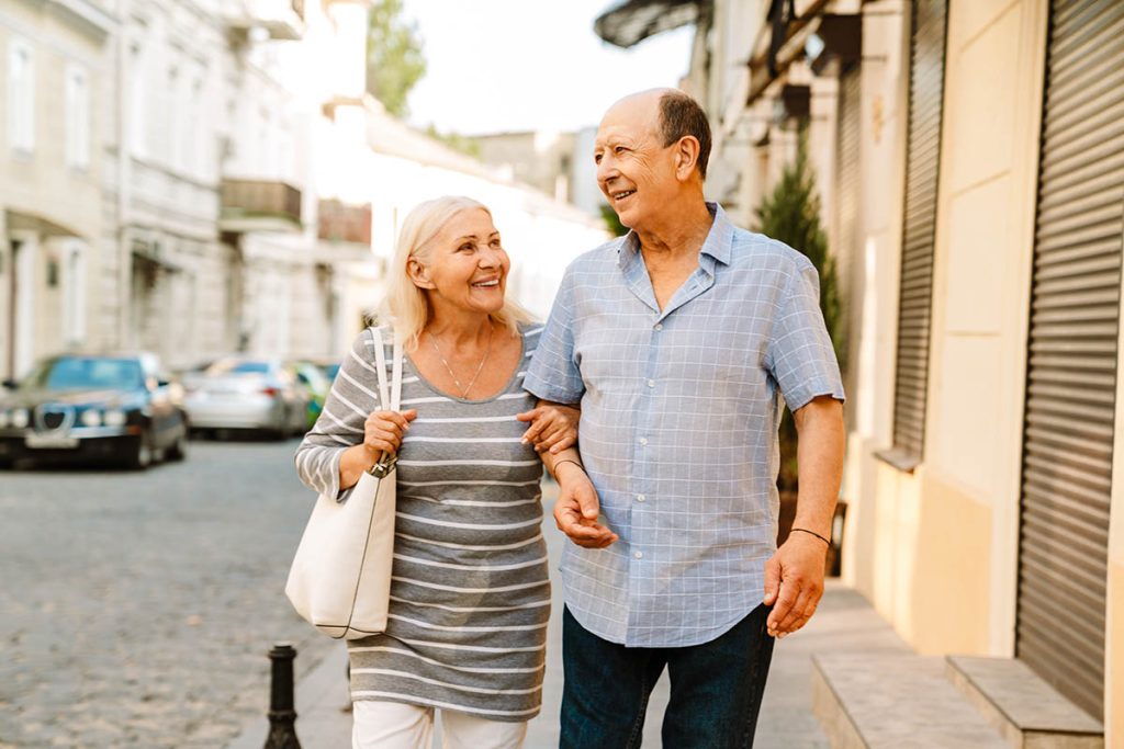senior couple holding hands and smiling while walking on city street