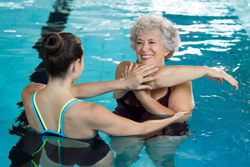older woman swimming exercising with instructor