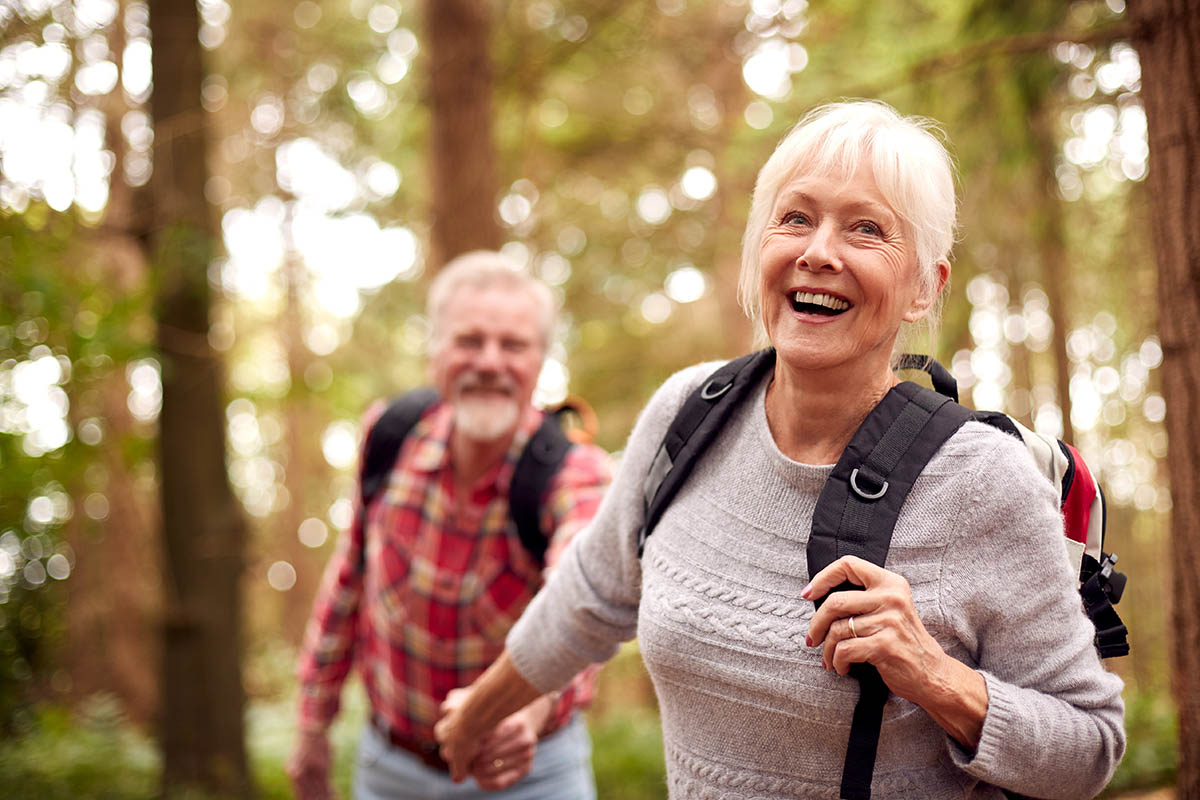 Loving Senior Couple Holding Hands Hiking In Woodland Countryside Together
