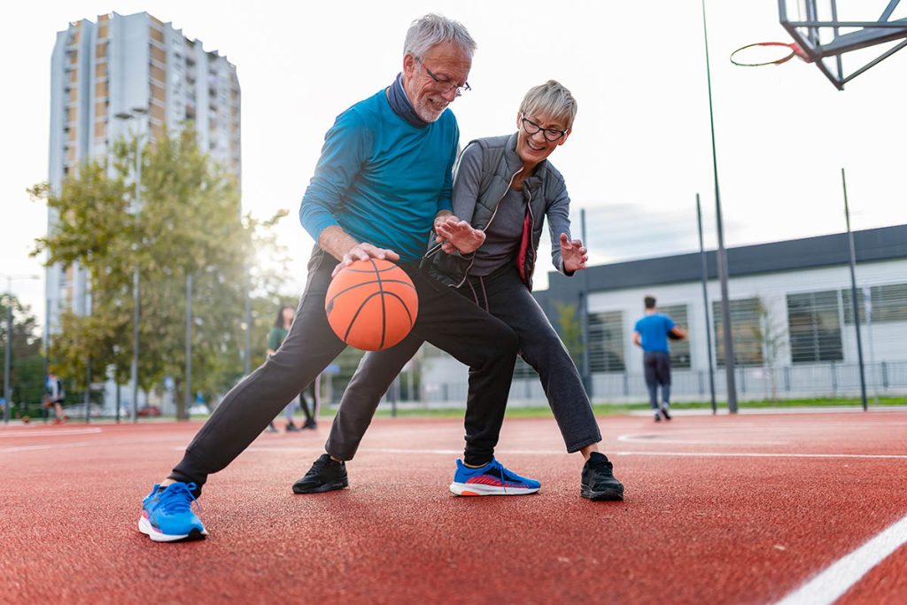 Cheerful active senior couple playing basketball on the urban basketball street court. Happy living after 60. S3niorLife