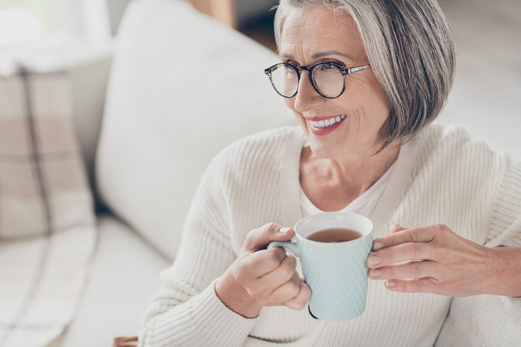 elderly lady wear white cardigan drinking coffee watching television indoors apartment room