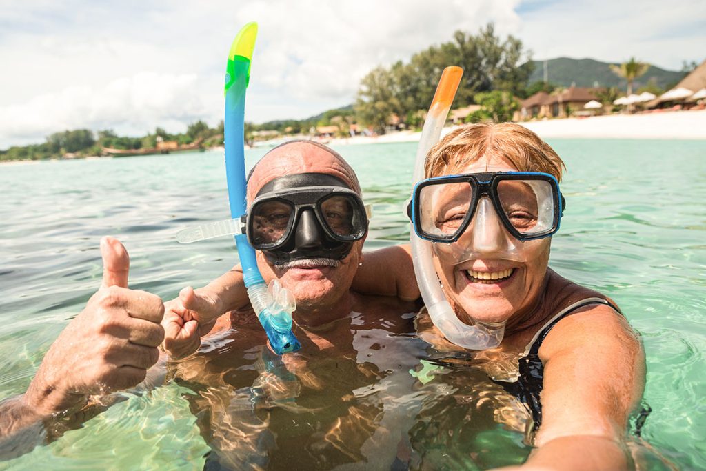 Senior happy couple taking selfie in tropical sea excursion with water camera - Boat trip snorkeling in exotic scenarios - Active retired elderly and fun concept around the world
