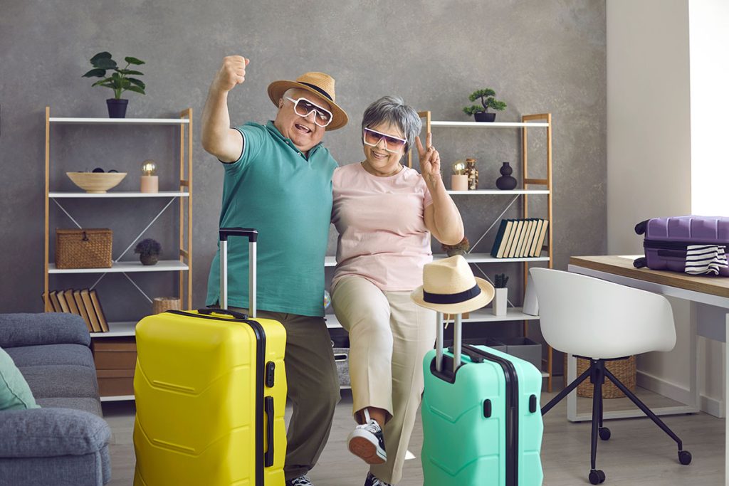 Active senior couple having fun at home before going on holiday trip. Portrait of happy aged husband and wife with packed travel suitcases ready for cool vacation together