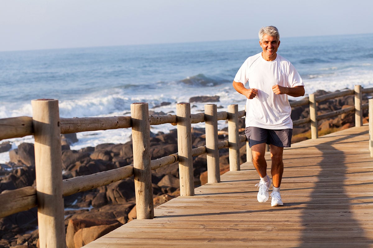 cheerful fit senior man running at the beach in the morning