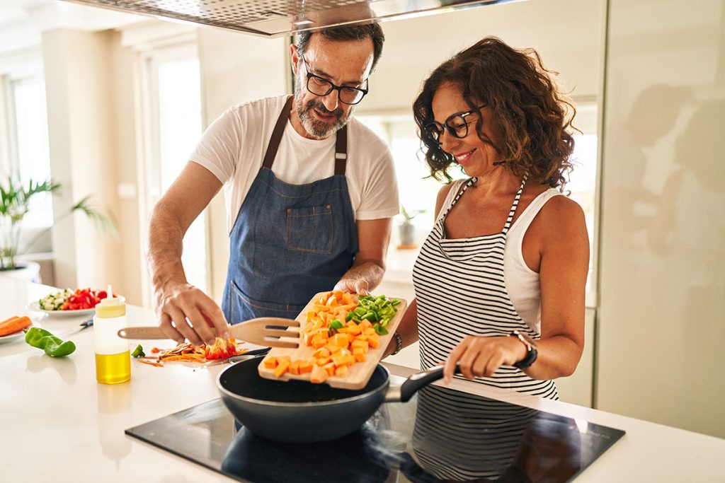 Middle age couple smiling confident pouring food on frying pan at kitchen