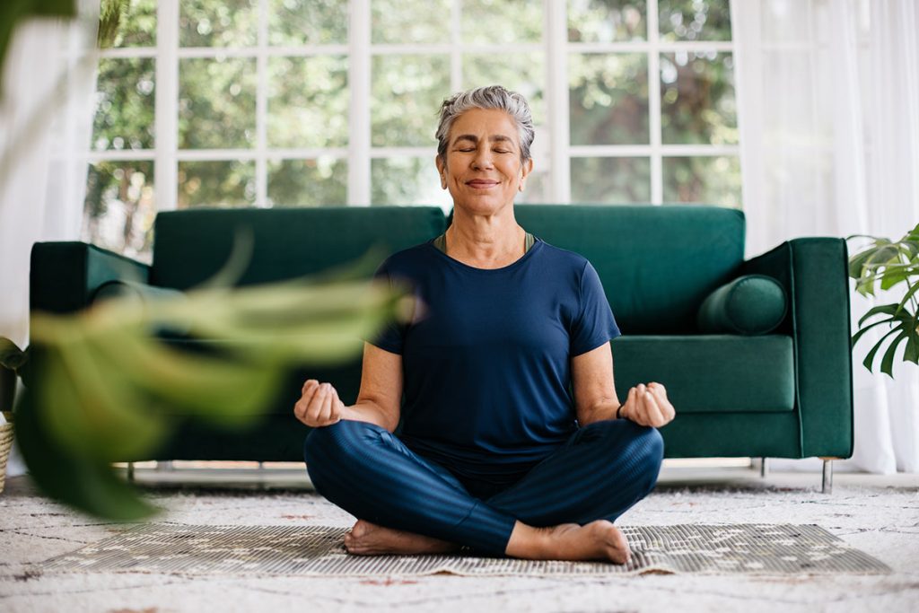 Senior woman meditating in lotus position at home