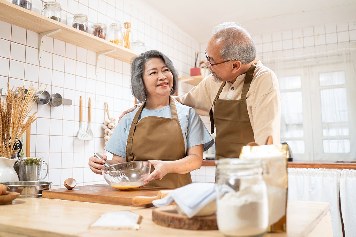 Senior elderly couple standing in kitchen at house feeling happy