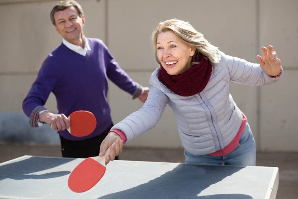 Happy active mature man and a woman playing table tennis