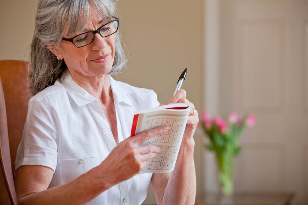 woman solving sudoku puzzles in a book with selective focus on the book.